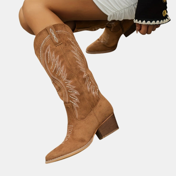 Tan cowboy boots with intricate white embroidery on a light gray background