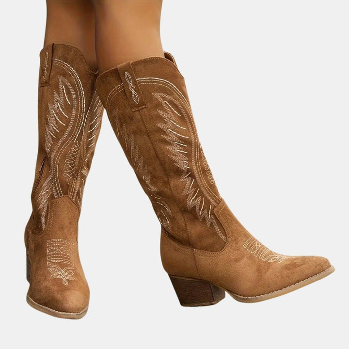 Brown cowboy boots with intricate white embroidery on a light gray background