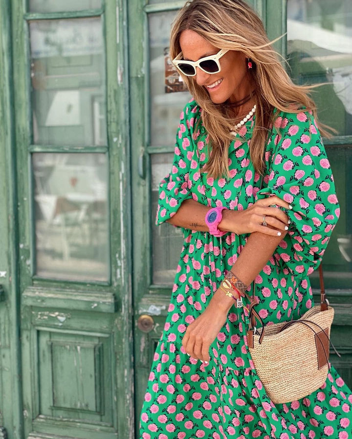 Woman wearing a green and pink dress with sunglasses and a watch, standing in front of a green door.