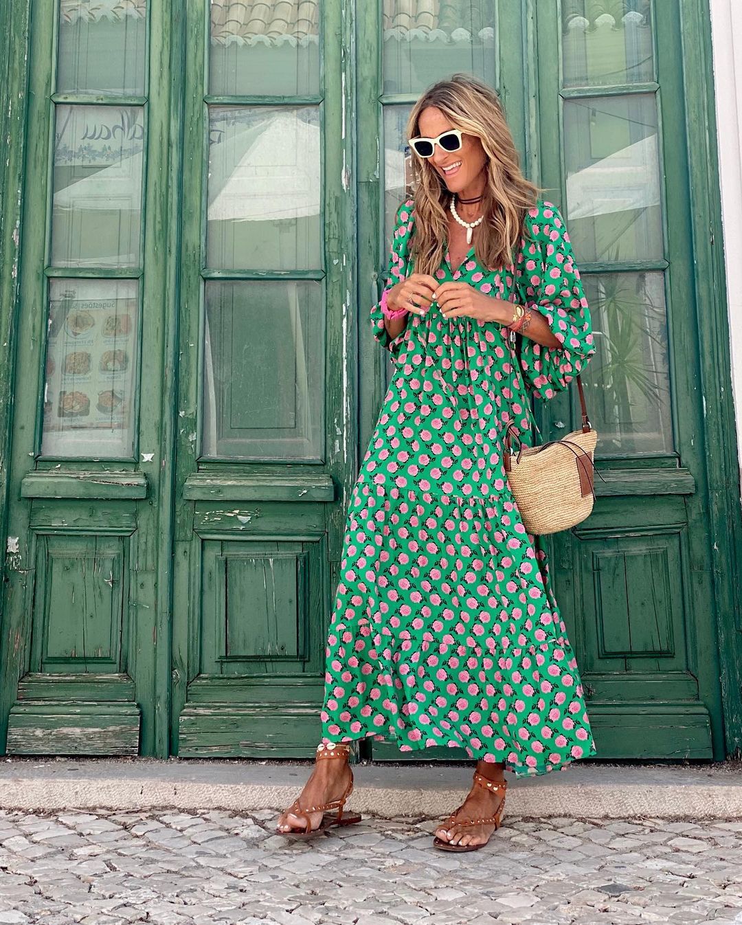Woman wearing a green floral dress with sunglasses and a handbag on a gray background