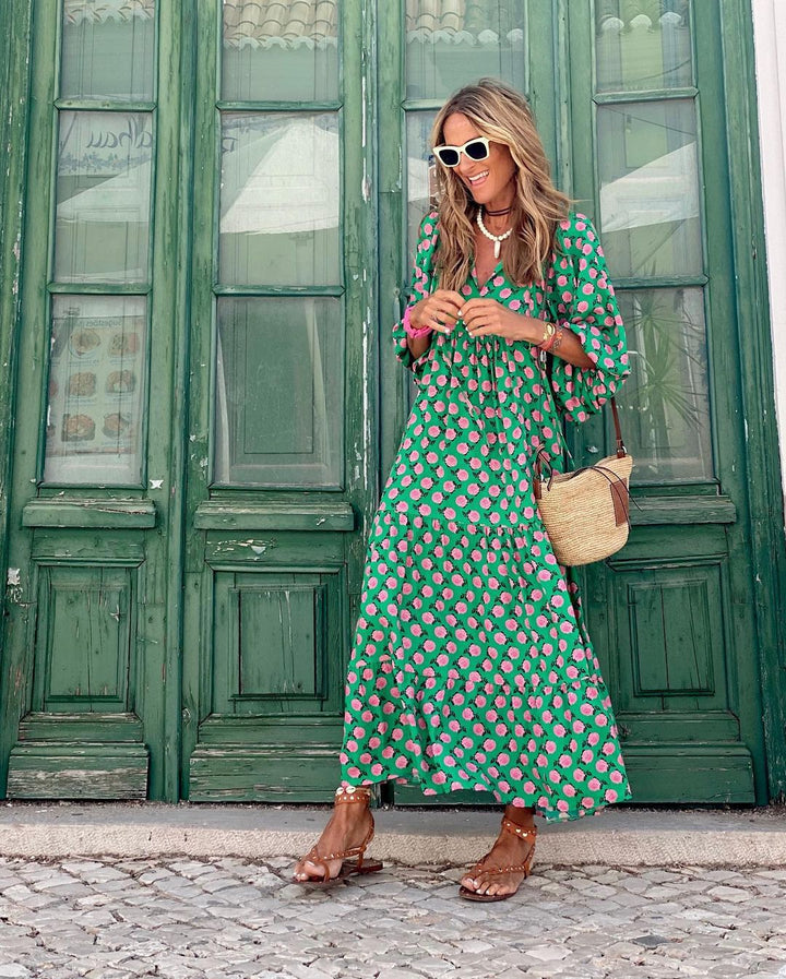 Woman wearing a green floral dress with sunglasses and a handbag on a gray background