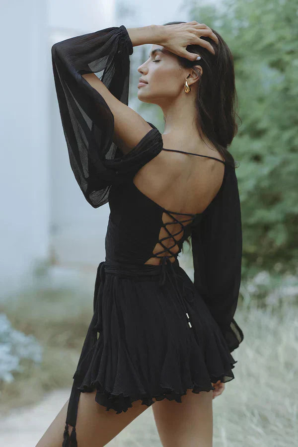 Woman wearing a black dress with sheer sleeves and lace-up back in a natural setting.