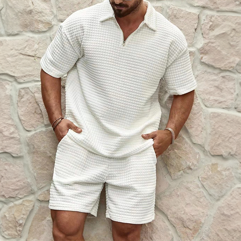 Man wearing a textured white outfit against a stone wall.