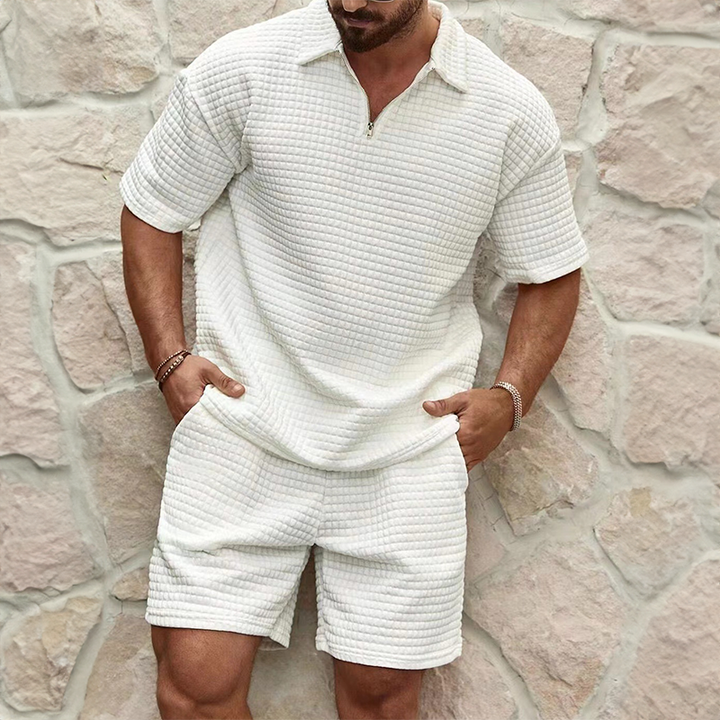 Man wearing a textured white outfit against a stone wall.