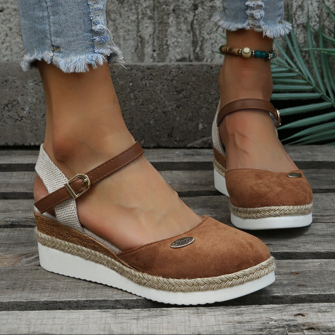 Brown wedge sandals with jute trim worn by a person on a wooden surface.
