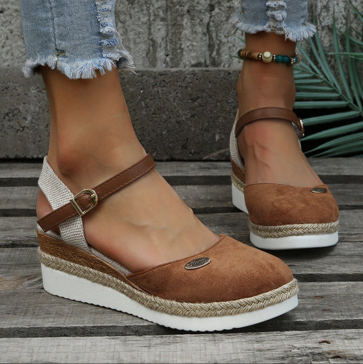 Brown wedge sandals with jute trim worn by a person on a wooden surface.