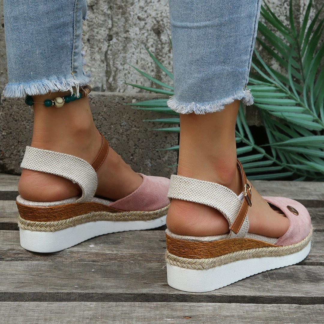 Close-up of feet wearing pink and white sandals with brown straps on a wooden floor.