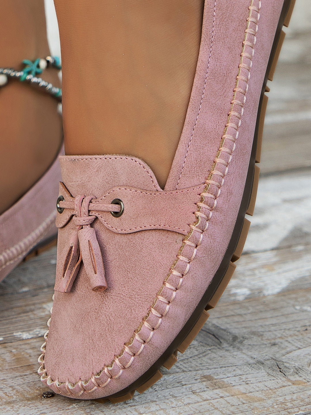 Pink suede loafer with tassel on a wooden floor