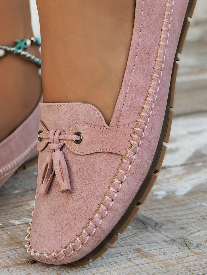 Pink suede loafer with tassel on a wooden floor
