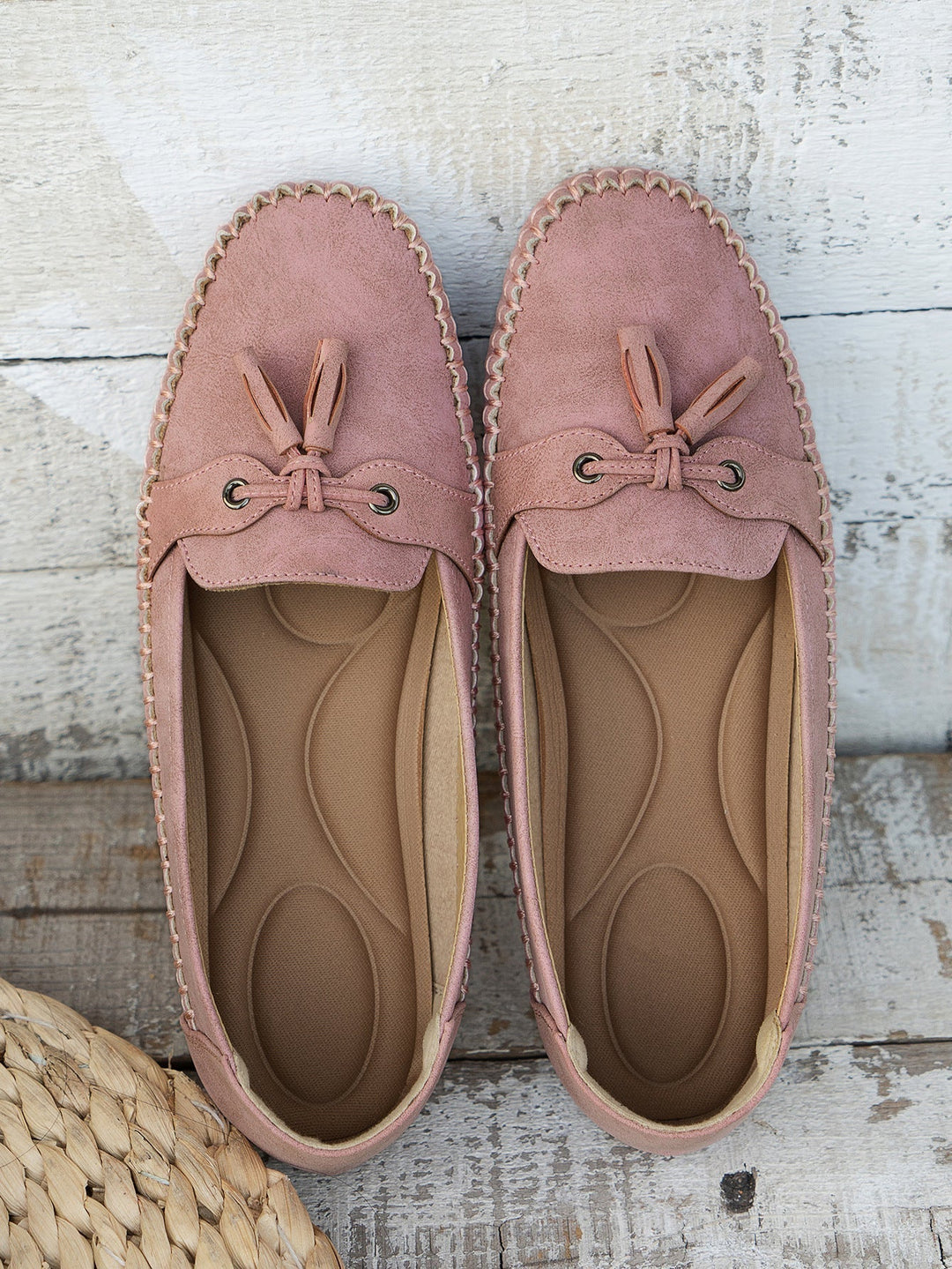 Pair of pink loafers with tassels on a wooden surface