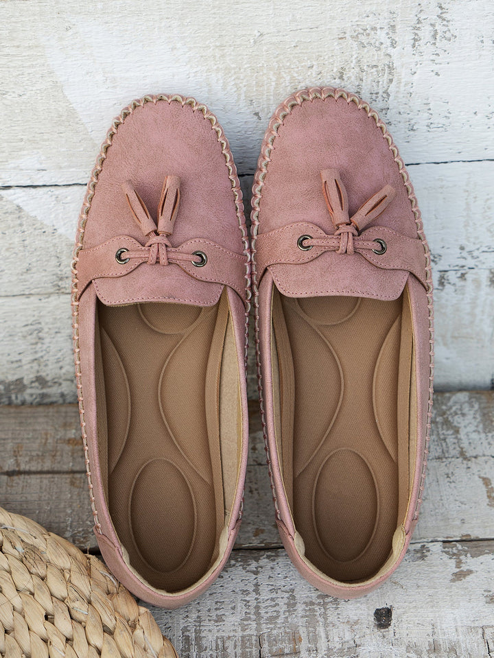 Pair of pink loafers with tassels on a wooden surface