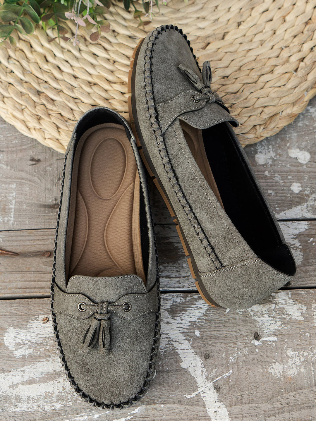 Pair of green loafers on a wooden surface with a woven mat in the background