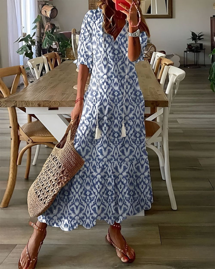 Woman in a blue patterned dress standing in a dining room.