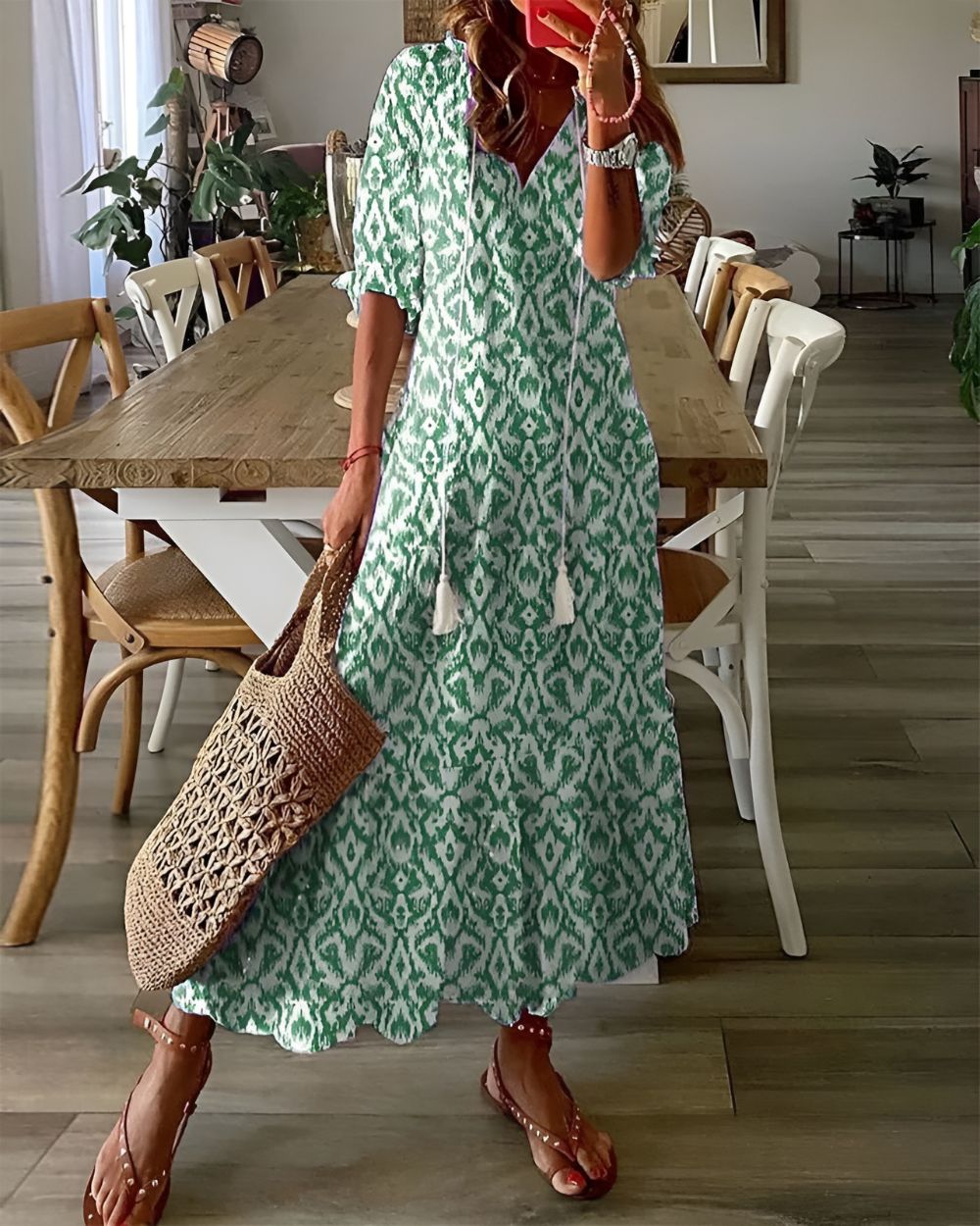 Woman in a green patterned dress holding a woven bag in a dining room.