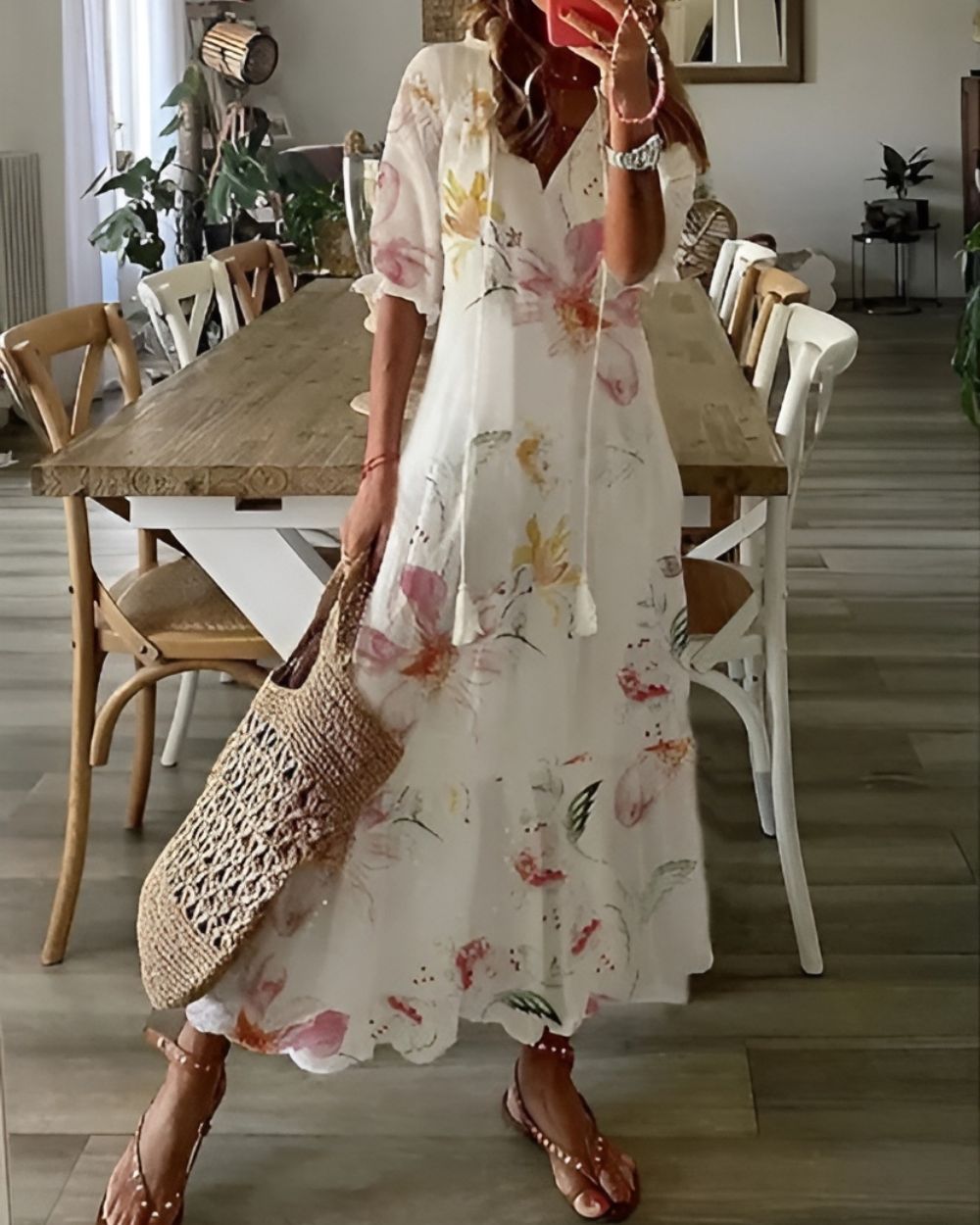 Woman in a floral dress holding a woven bag in a dining room.