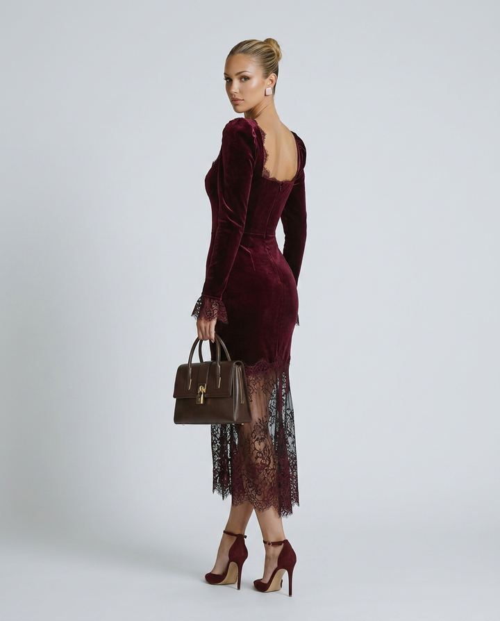 Woman wearing a burgundy velvet dress with lace details, holding a matching handbag on a white background.