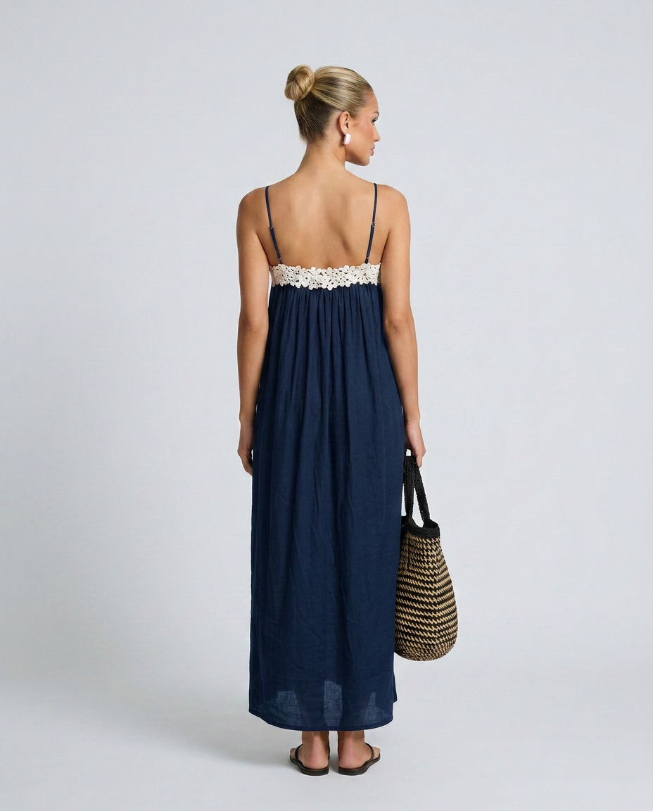 Woman wearing a navy blue dress with white lace trim, holding a straw bag on a light gray background
