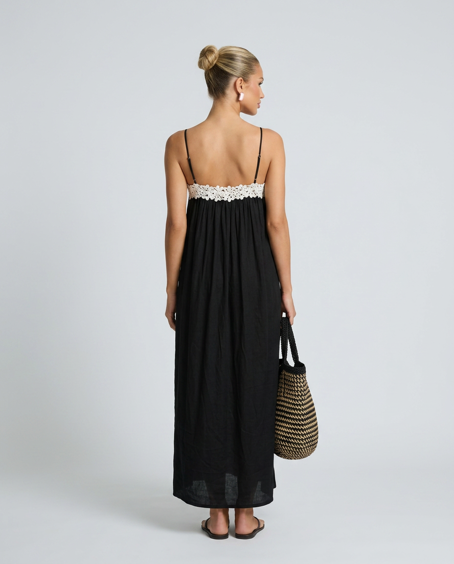 Woman wearing a black dress with white lace trim, holding a straw bag on a plain background