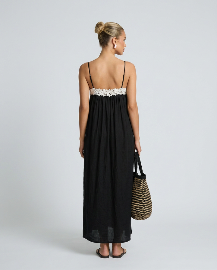 Woman wearing a black dress with white lace trim, holding a straw bag on a plain background