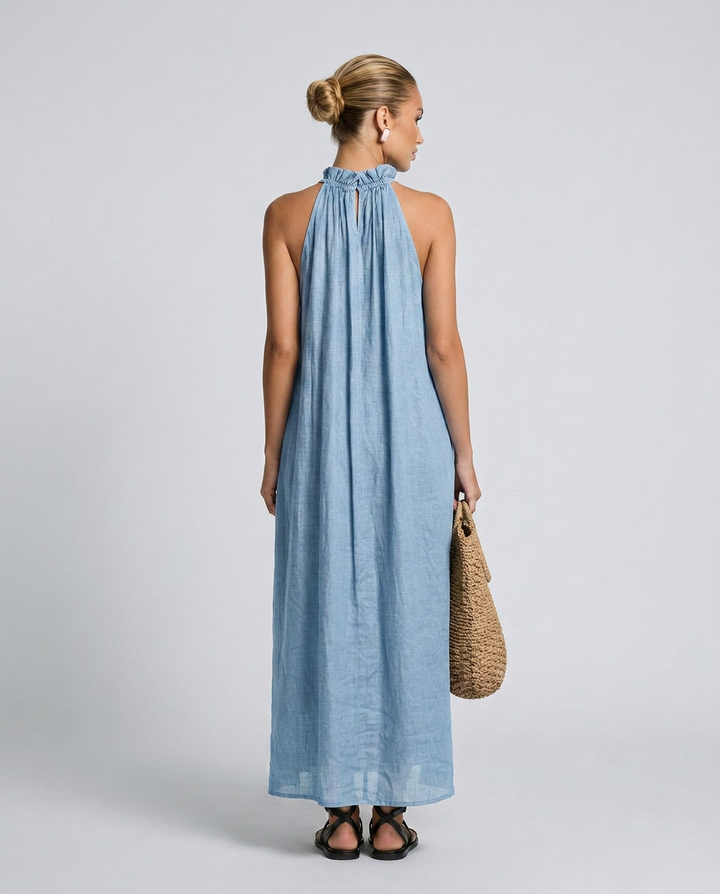 Woman wearing a light blue dress holding a woven bag on a plain background