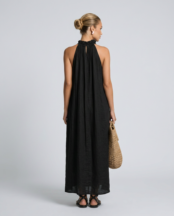 Woman wearing a black halter neck dress holding a woven bag on a plain background