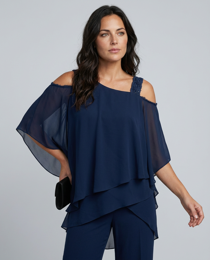 Woman wearing a navy blue outfit with sheer sleeves on a gray background