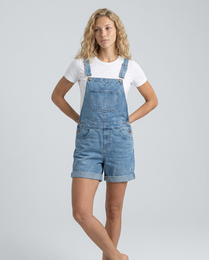 Woman wearing denim overalls and a white t-shirt on a gray background