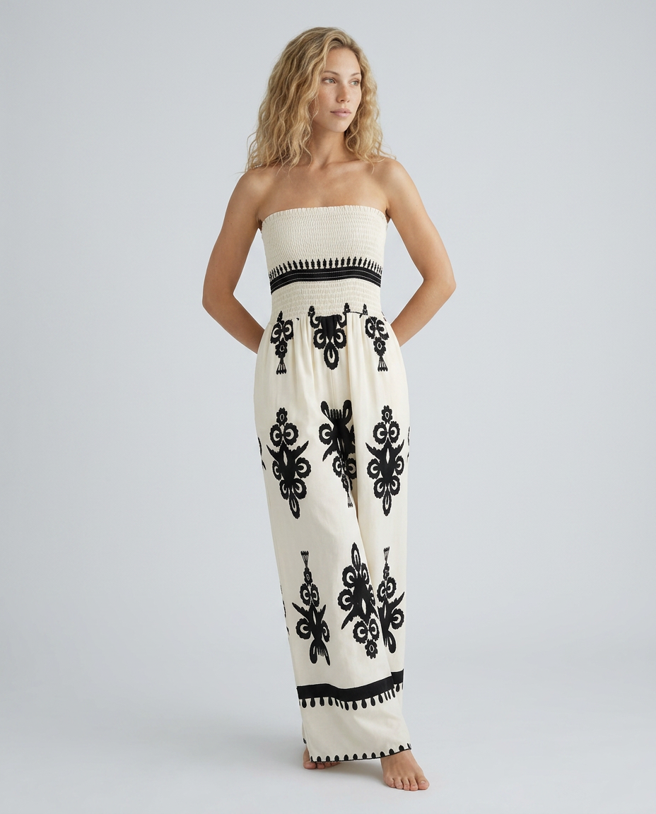 Woman wearing a strapless jumpsuit with black patterns on a plain background