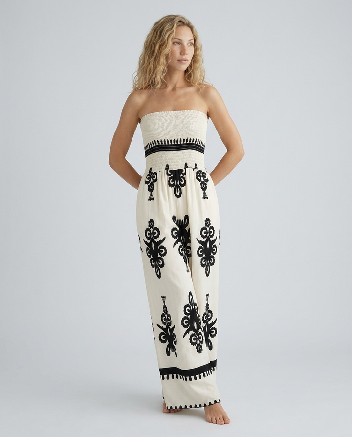 Woman wearing a strapless jumpsuit with black patterns on a plain background