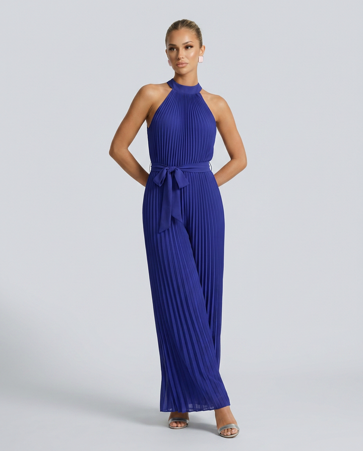 Woman wearing a blue pleated jumpsuit on a gray background