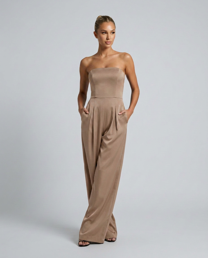 Woman wearing a strapless beige jumpsuit on a plain background