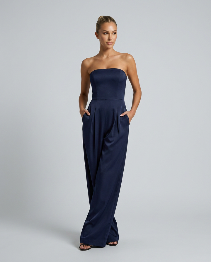 Woman wearing a strapless navy jumpsuit on a gray background