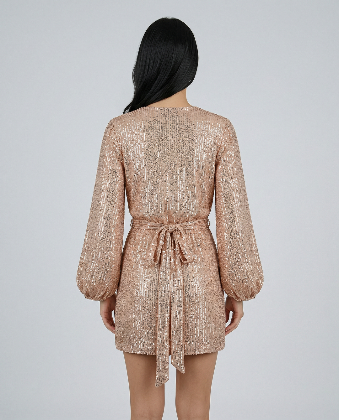 Back view of a person wearing a sparkly gold dress on a light gray background
