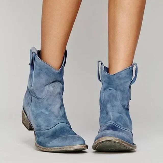 Blue suede cowboy boots worn by a person on a plain background