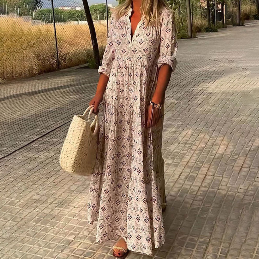 Woman in a long patterned dress holding a straw bag on a paved walkway.