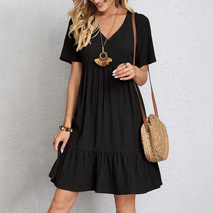 Woman wearing a black dress holding a straw bag against a light gray background