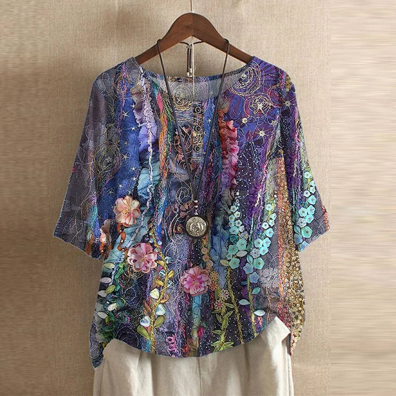 Colorful floral and abstract patterned top on a wooden hanger against a beige wall.