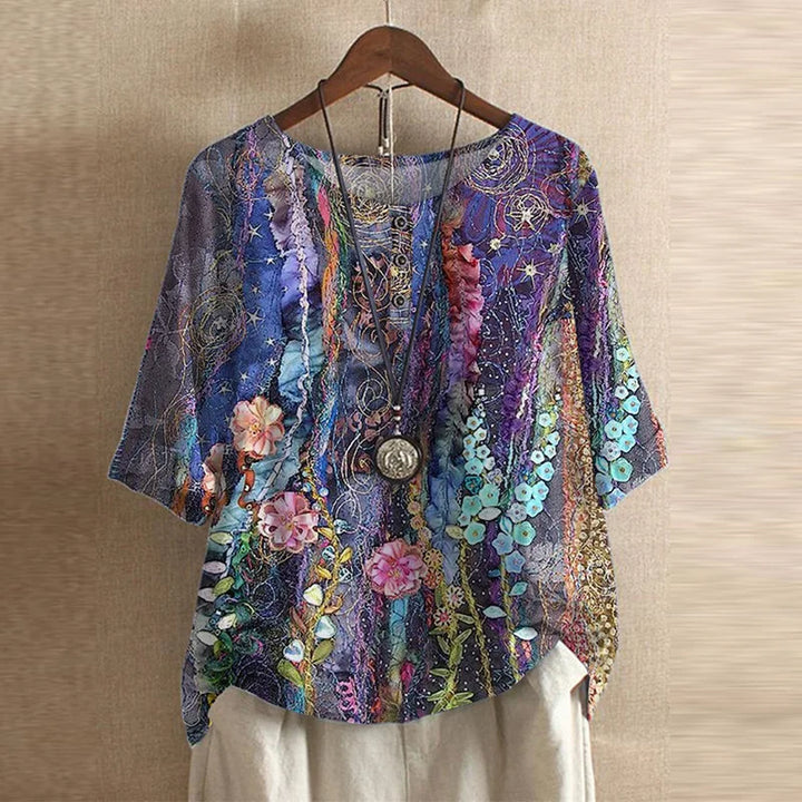 Colorful floral and abstract patterned top on a wooden hanger against a beige wall.