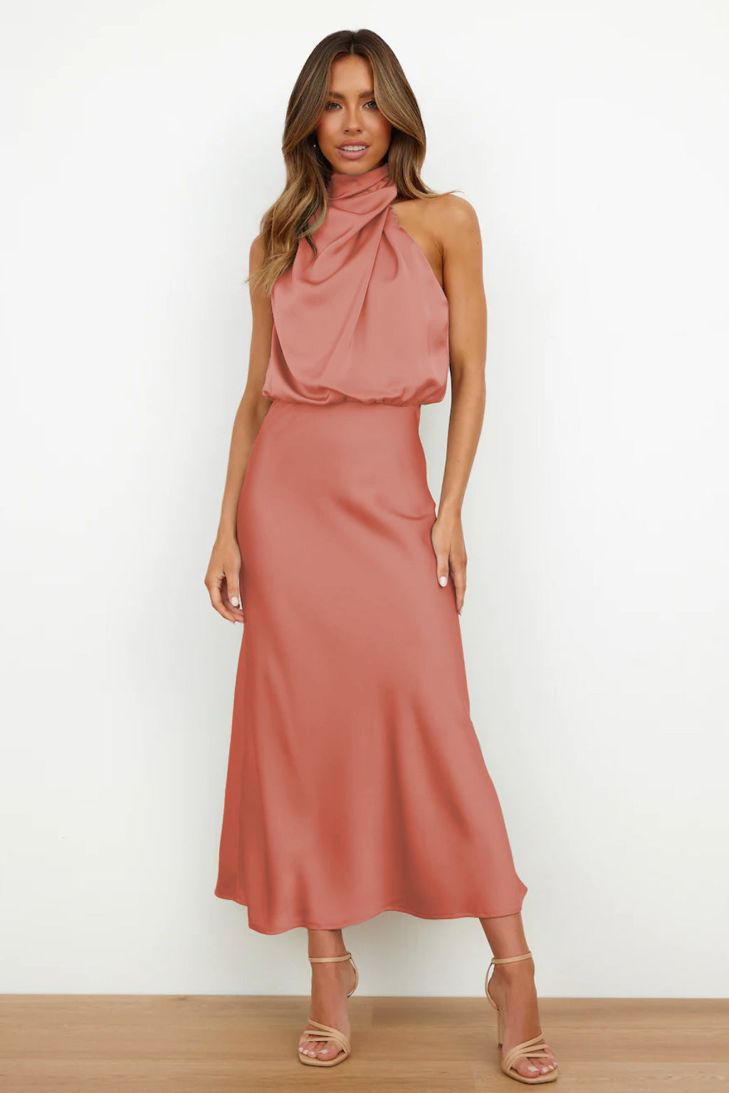 Woman wearing a pink halter neck dress against a white background