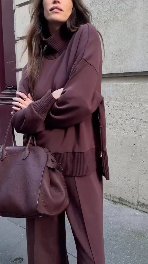 Person wearing a brown outfit with a matching handbag against a neutral background