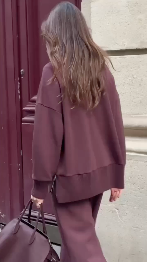 Person wearing a mauve outfit walking past a red door.