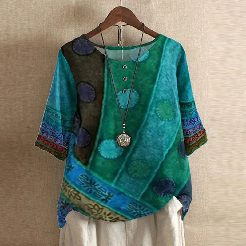 Colorful textured top with patterns and a necklace on a hanger against a beige wall.
