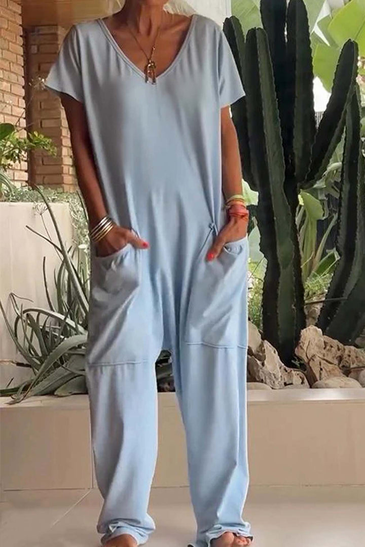 Person wearing a light blue jumpsuit standing outdoors with plants in the background