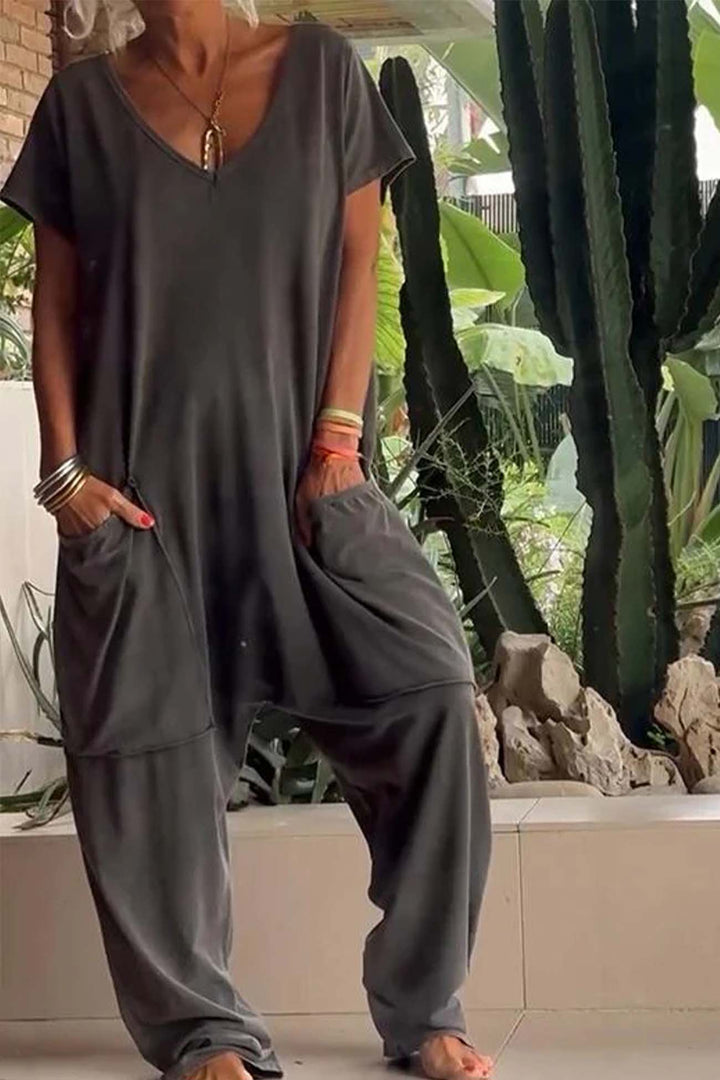 Person wearing a gray outfit with wide-leg pants in an outdoor setting with plants.