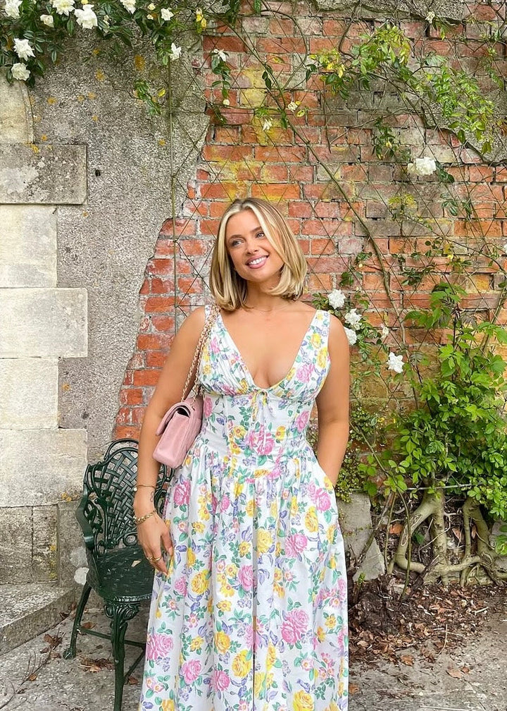 Woman in a floral dress standing in front of a brick wall with greenery