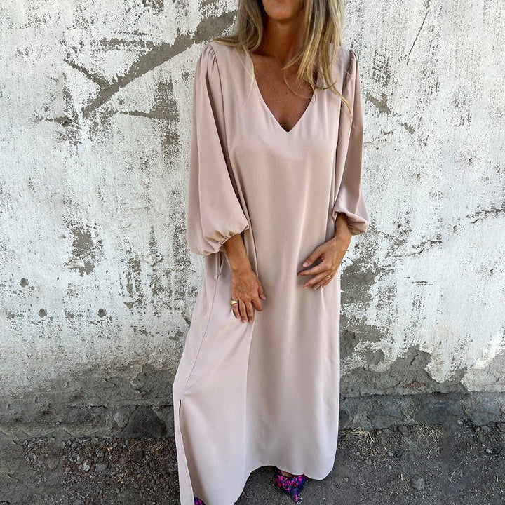 Woman wearing a beige dress against a textured wall.