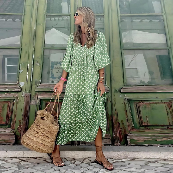 Woman in a green patterned dress standing in front of a green building.