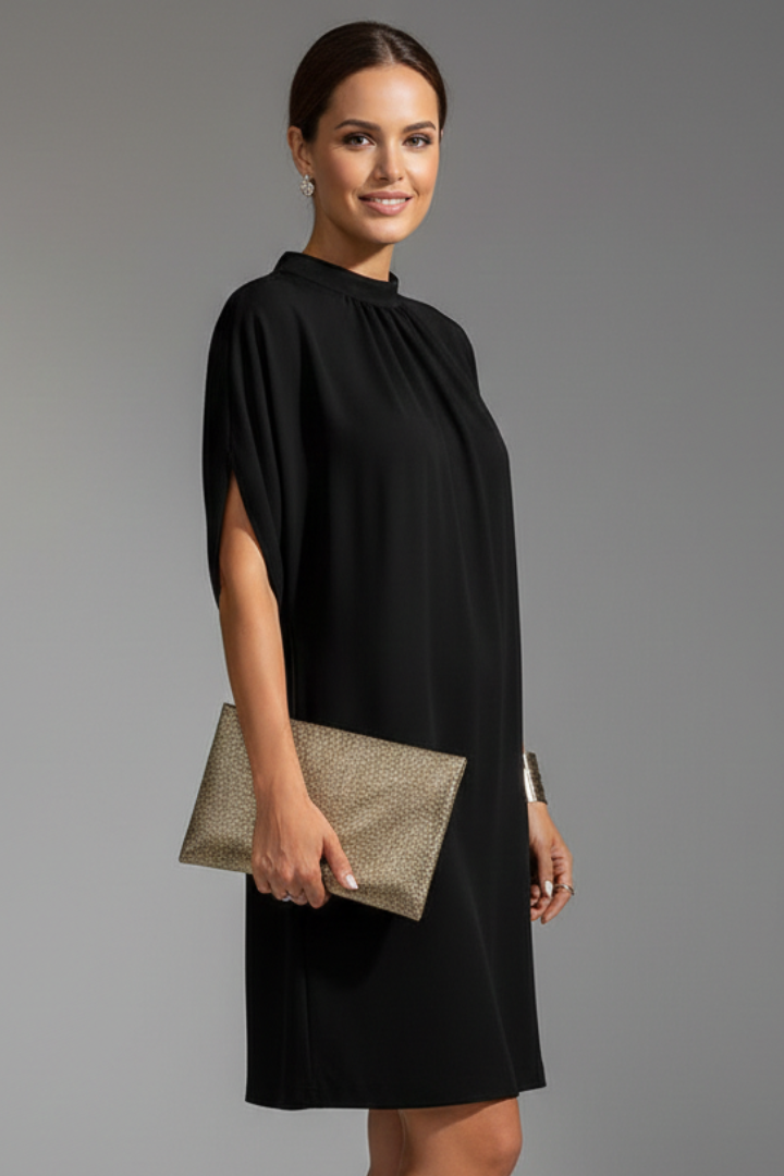 Woman wearing a black dress holding a gold clutch against a gray background