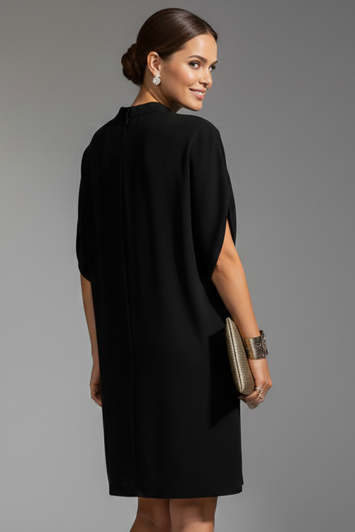 Woman wearing a black dress holding a clutch against a gray background