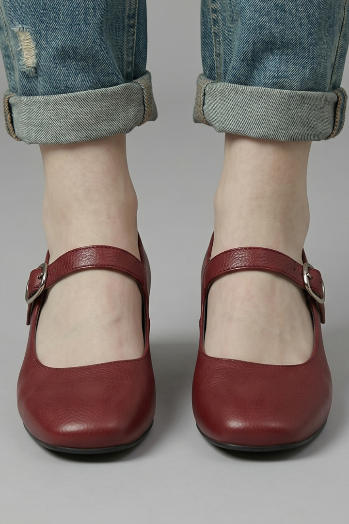 Red shoes worn with rolled-up jeans on a neutral background